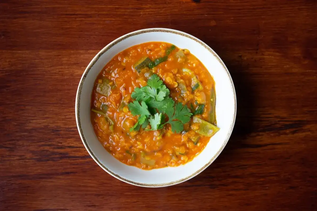 Un plato de lentejas al curry, con cilantro fresco, servido en un cuenco blanco sobre una mesa de madera.