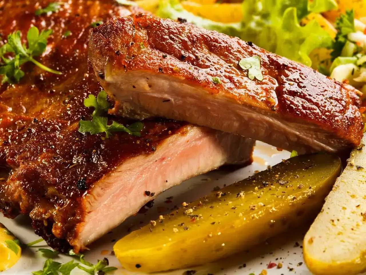 Costillas al horno con patatas, jugosas y doradas, acompañadas de ensalada fresca y pepinillos. ¡Un festín para los sentidos!