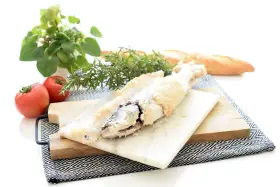 Lubina a la sal lista para servir, acompañada de tomates frescos, romero y pan rústico.