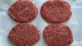 Cuatro hamburguesas de carne poco hecha, listas para cocinar y disfrutar.