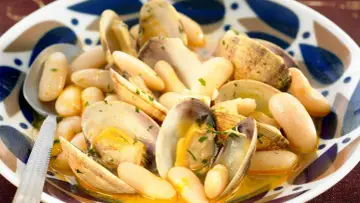Un plato humeante de fabes con almejas, con judías blancas tiernas y almejas jugosas en una salsa dorada, adornado con perejil picado.