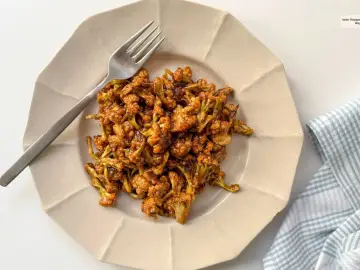Coliflor glaseada, una de las mejores recetas con coliflor. Servida en plato beige con tenedor plateado y servilleta a cuadros.