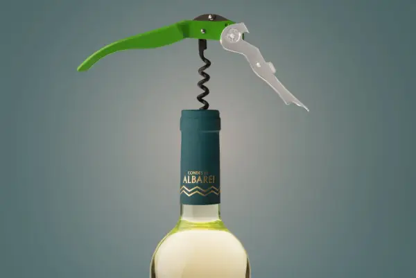 Sacacorchos verde y plateado sobre una botella de vino blanco "Condes de Albarei". El sacacorchos está listo para extraer el corcho, recordándonos de donde viene el corcho.