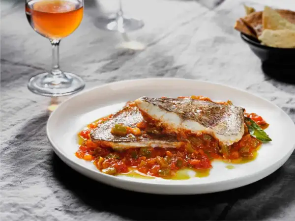 Deliciosa urta a la roteña servida en plato blanco, con vino y pan tostado al fondo.