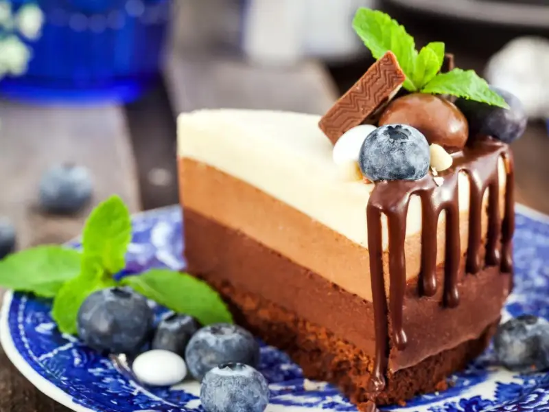 Deliciosa tarta de tres chocolates, con capas de chocolate blanco, con leche y negro, decorada con arándanos y menta.