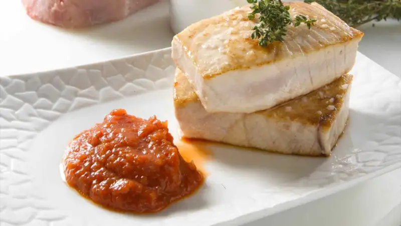 Dos trozos de atún a la plancha apilados, con una cucharada de salsa de tomate y una ramita de tomillo.