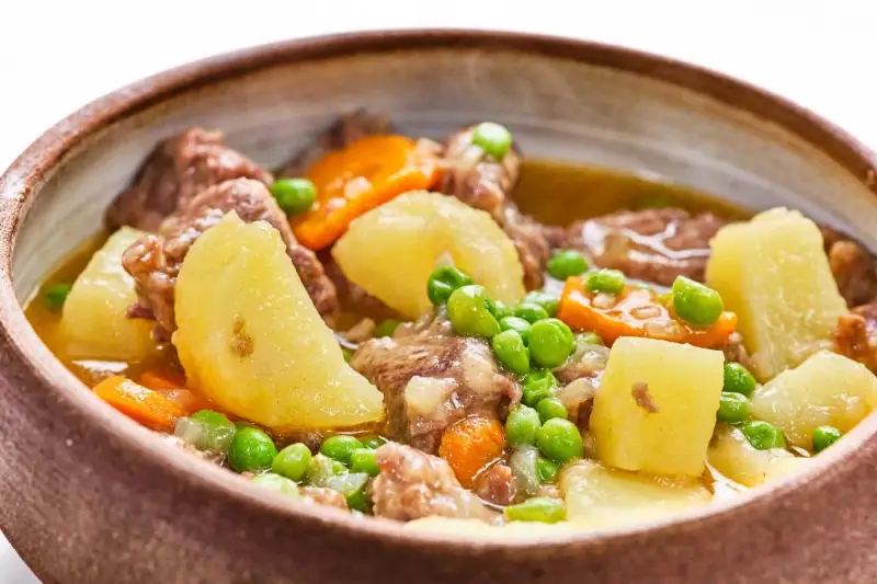 Un reconfortante ragú con trozos de carne tierna, patatas, zanahorias y guisantes en un cuenco rústico.