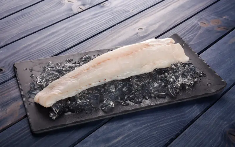 Filete de pescado rosado fresco sobre hielo picado en una tabla negra, listo para cocinar.