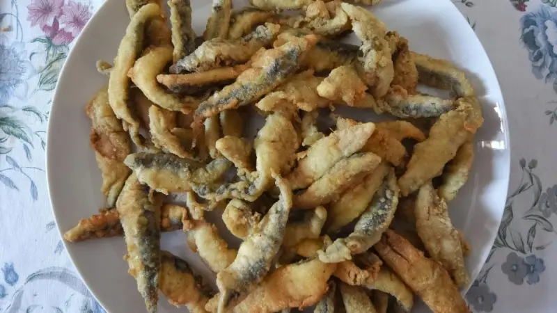 Un plato blanco lleno de boquerones fritos crujientes, listos para disfrutar.