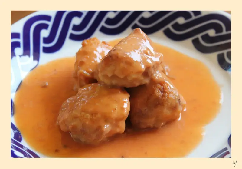 Deliciosas albóndigas de rape en una cremosa salsa naranja, servidas en un plato con borde azul.