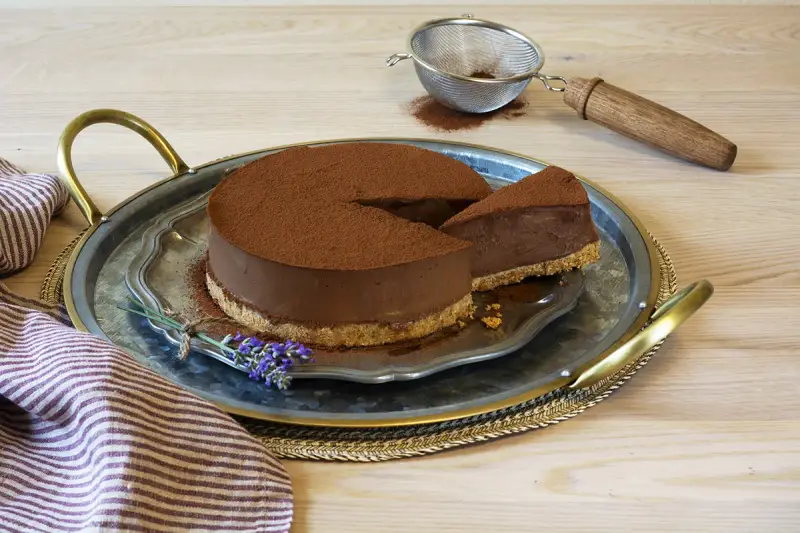 Delicioso pastel de chocolate cubierto de cacao, con una rebanada servida en una bandeja de plata, decorado con lavanda.