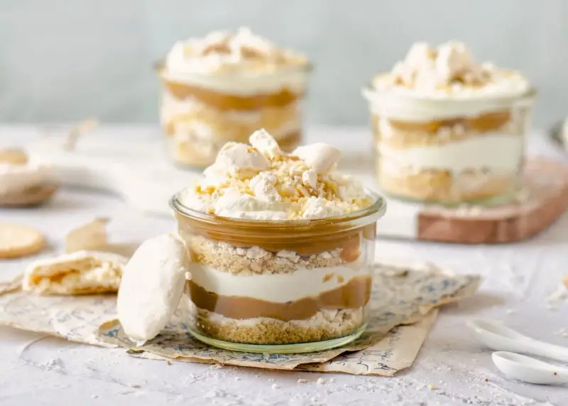 Postres en vaso con capas de bizcocho, crema y dulce de leche, coronados con merengue y polvito canario.